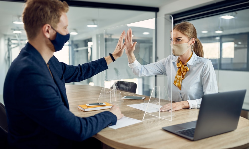 Coworkers high five through partition